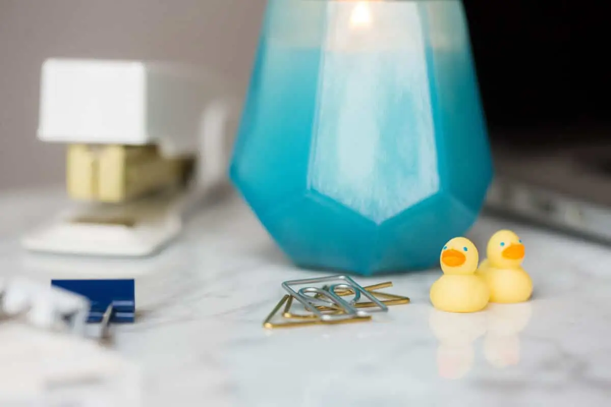 white stapler, blue candle, and mini rubber ducks sit on top of a desk with binder clips and paper clips