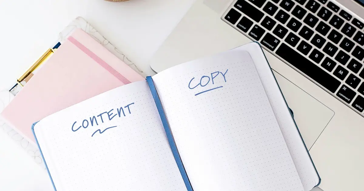 An open notebook sitting on top of a laptop keyboard. On one page of the notebook, "content" is written and "copy" is written on the other page.