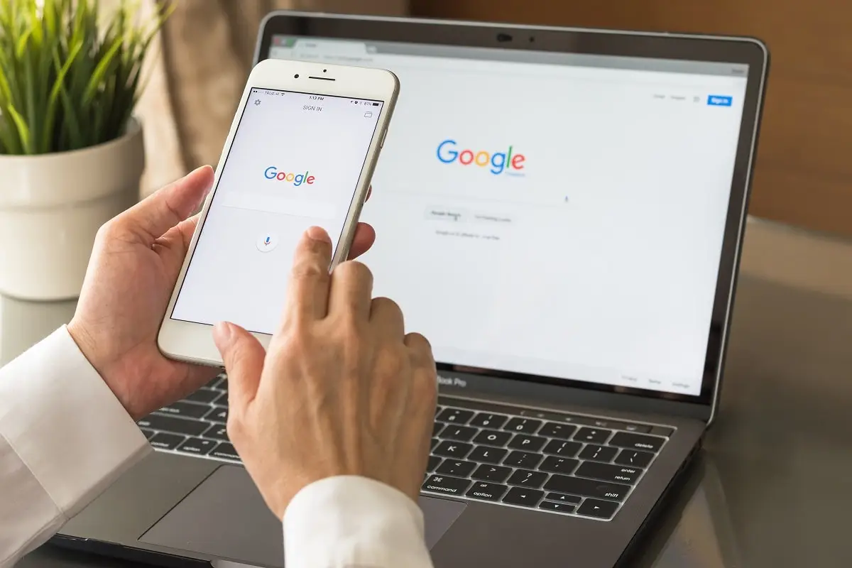 Google search engine sign up page on mobile app touchscreen on iphone in business person's hand and on computer screen display. The person is ready to use G Suite