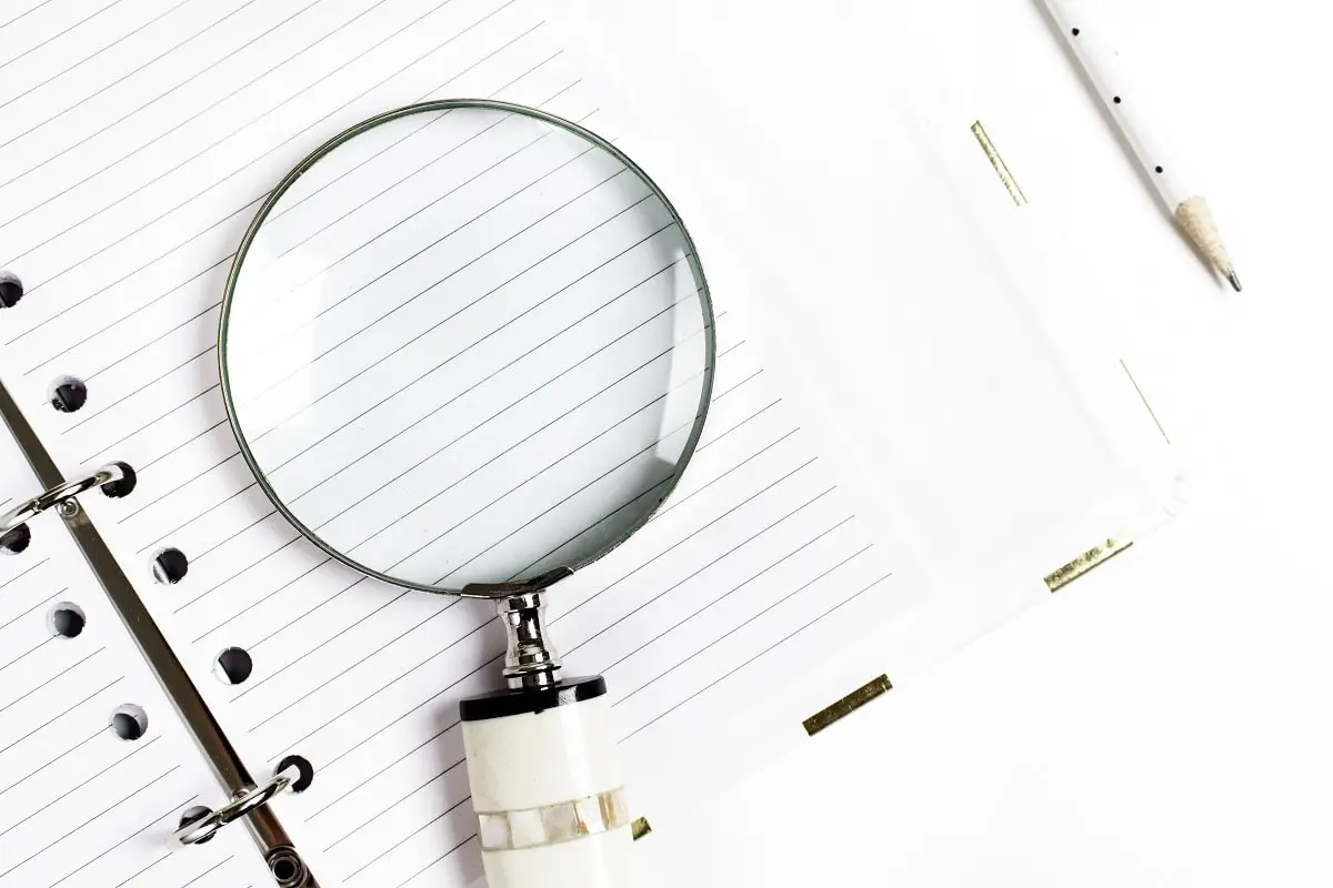 A magnifying glass on top of a lined notebook next to a pencil.