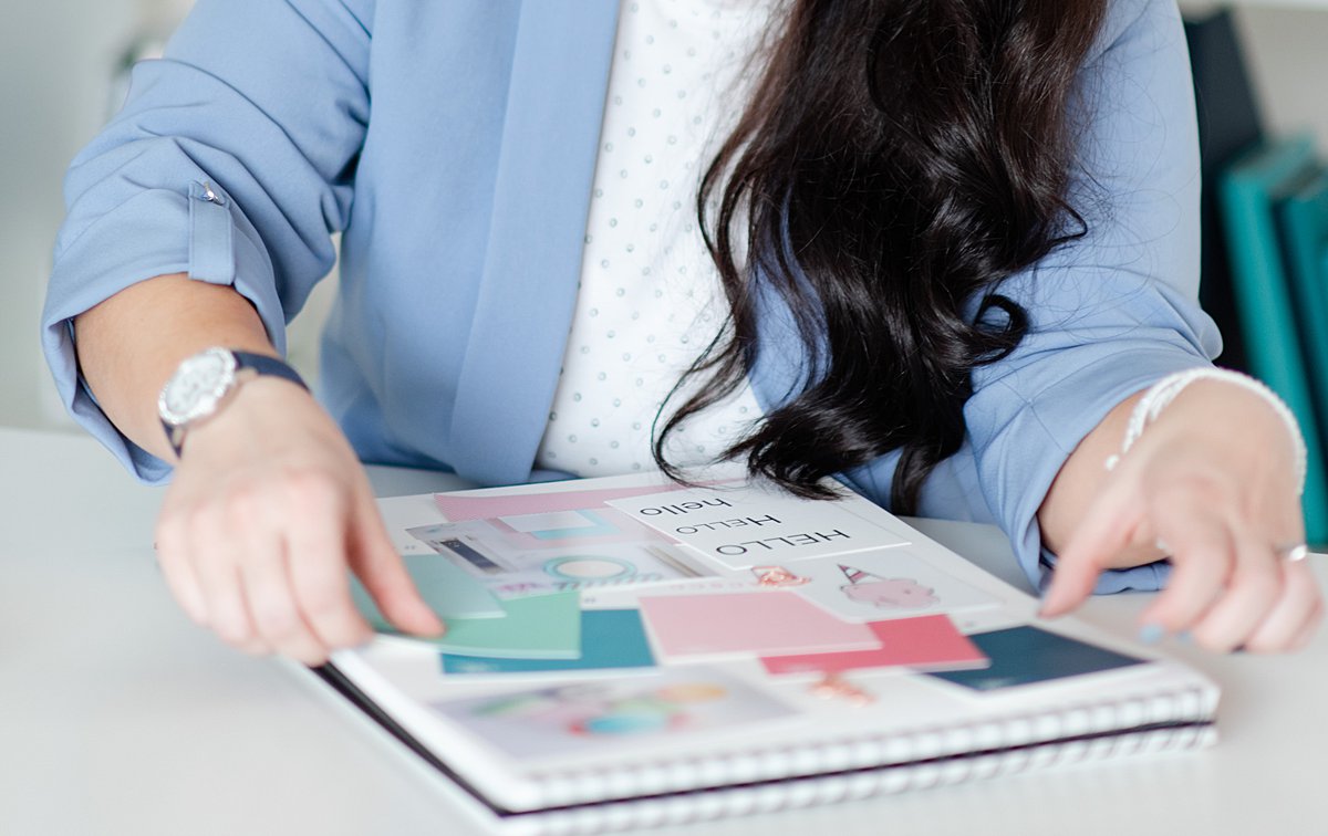A woman looking at color swatches and font type examples of a branding kit on a tabletop.