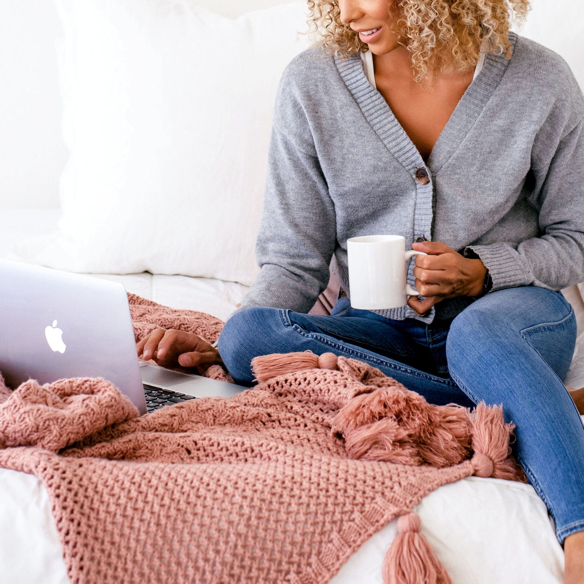 Woman holding a cup of coffee and working on her laptop to choose the best sidebar widgets for her website's blog
